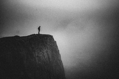 Silhouette person standing on rock against sky