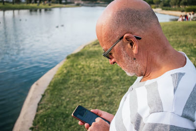 Midsection of man using mobile phone at lake