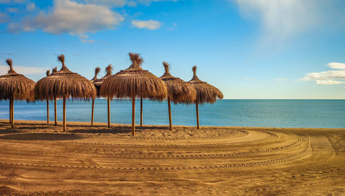 Thatched roof umbrellas on beach against sky