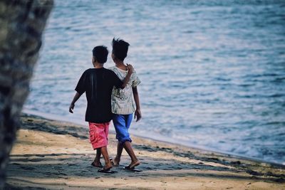 Full length of friends walking on shore at beach