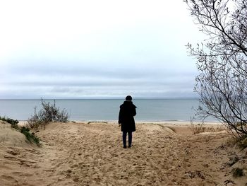 Rear view of man standing at beach against sky at palanga