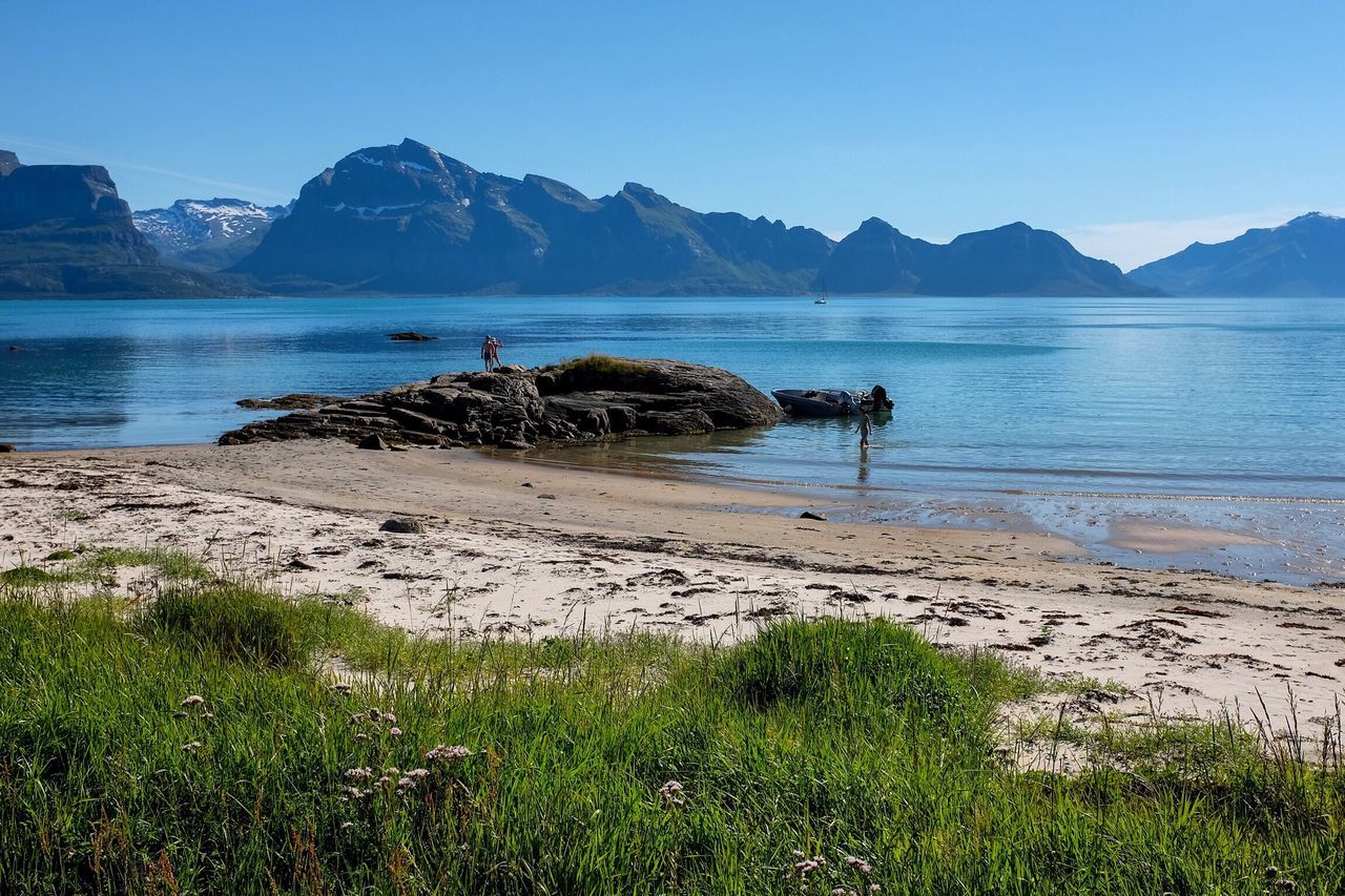 water, mountain, clear sky, tranquil scene, tranquility, scenics, beauty in nature, mountain range, nature, shore, blue, idyllic, coastline, grass, sky, non-urban scene, outdoors, day, non urban scene, remote, no people, calm, plant, lakeshore, landscape, travel destinations, tourism, growth