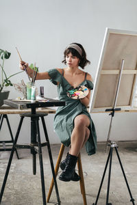 Young woman painting on canvas while sitting on table