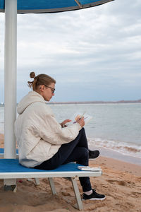 Young woman artist painting or doing travel sketches using watercolor by the seaside