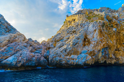 Old ruins on rocky mountain at sea shore against sky