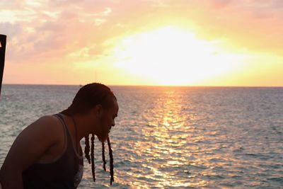 Side view of young woman standing at beach during sunset