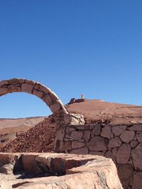 Arch by wall at desert against blue sky