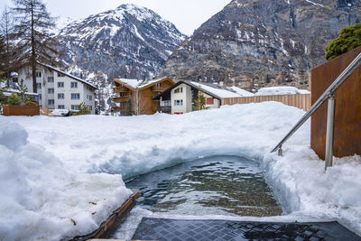 Small hot pool surrounded by snow with view of houses and mountains from resort