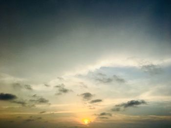 Low angle view of sunlight streaming through clouds during sunset