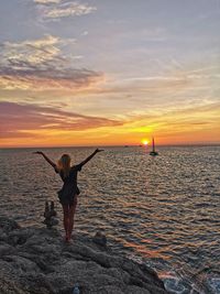 Woman standing on rock by sea against sky during sunset