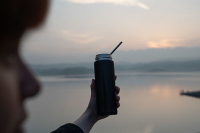 Midsection of woman holding umbrella against sea during sunset