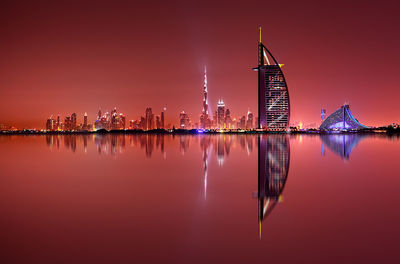 Reflection of illuminated burj al arab hotel and buildings on sea at night