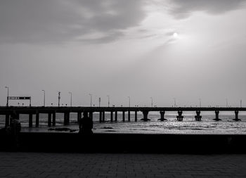 Silhouette people on pier by sea against sky