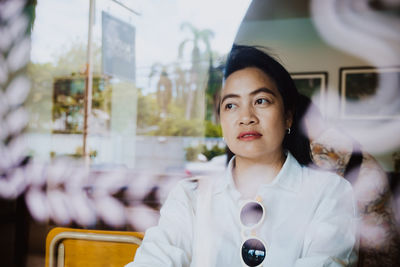 Thoughtful woman looking away seen through glass window