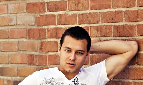 Portrait of man with hand behind head against brick wall