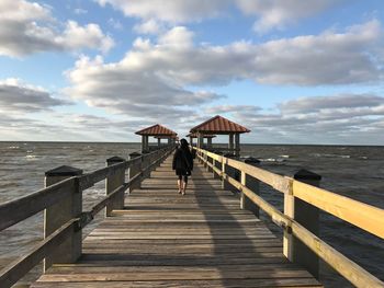 Woman walking on pier over sea against sky