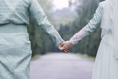 Midsection of couple holding hands against tree