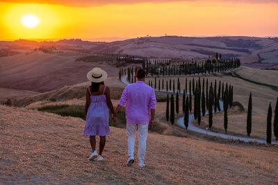 Rear view of women walking on field against sky during sunset