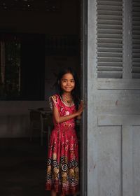 Portrait of smiling young woman standing against door