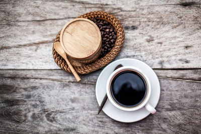 High angle view of black coffee with beans on wooden table