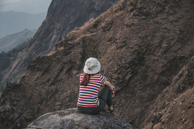 Rear view of woman sitting on rock