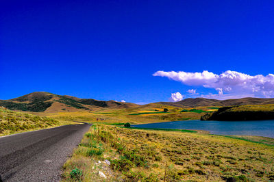 Scenic view of road by mountains against blue sky