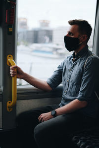 Close-up of mid adult man wearing mask sitting in bus