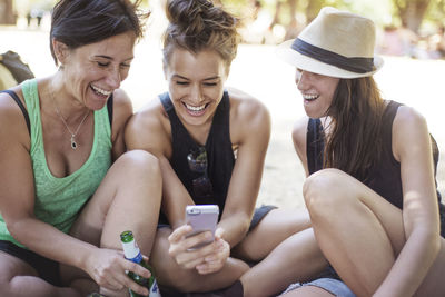 Cheerful female friends looking at phone while enjoying in park