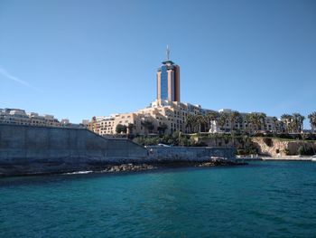 View of buildings by sea against clear blue sky