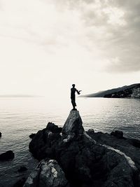 Man standing on rock by sea against sky