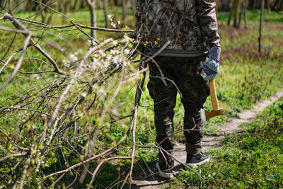 Low section of man carrying cut branches and axe in forest