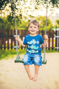 Portrait of smiling boy sitting on swing at playground