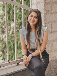 Portrait of young woman sitting on railing