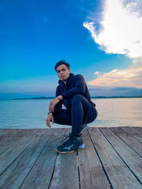 Portrait of young man sitting on wood against sea