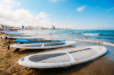Surfboards moored on beach against sky