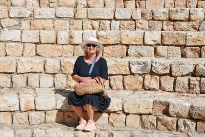 Portrait of woman using laptop while standing against brick wall