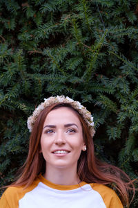 Thoughtful woman wearing tiara while smiling against plants