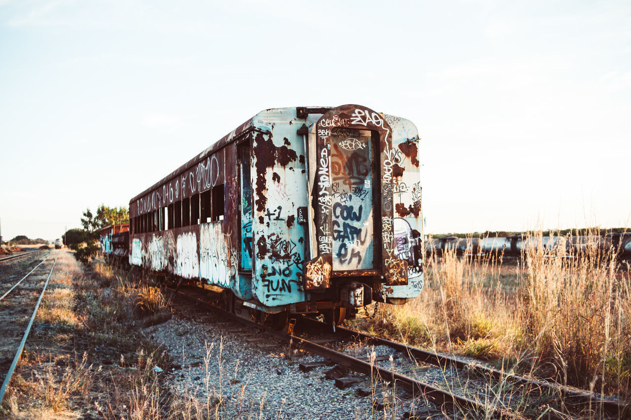 ABANDONED TRAIN ON RAILROAD TRACK AGAINST SKY