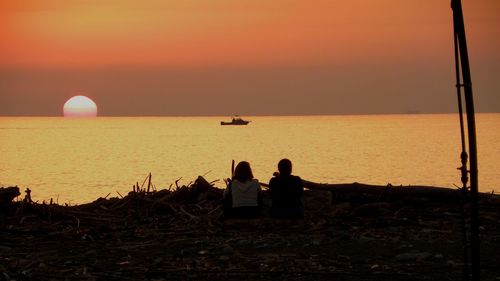 Silhouette people on sea shore against sky during sunset