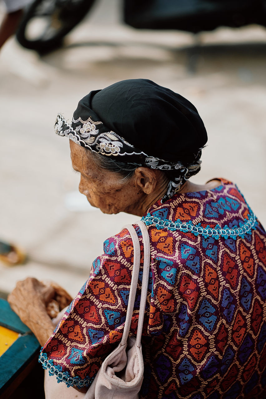 focus on foreground, one person, real people, adult, day, clothing, lifestyles, women, rear view, leisure activity, sitting, senior adult, casual clothing, senior women, close-up, hat, traditional clothing, outdoors, multi colored, hairstyle, scarf