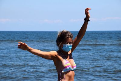 Woman with arms raised on beach against sky