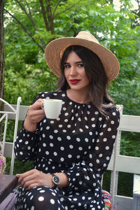 Portrait of smiling young woman drinking coffee while sitting at porch 