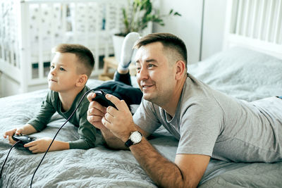 Father and son playing video game while lying down on bed