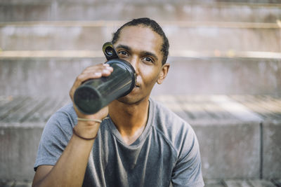 Portrait of man drinking protein from shaker while sitting on steps