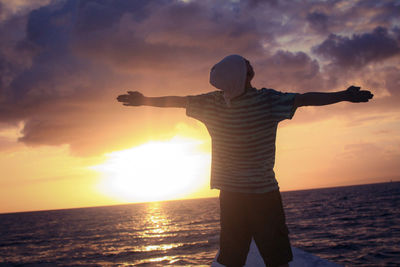 Rear view of man standing at sea shore during sunset
