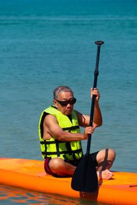 Full length of man sitting on paddleboard in sea