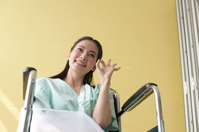 Smiling disabled woman gesturing while sitting on wheelchair against wall