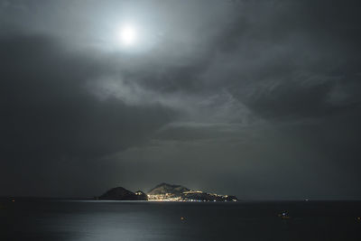 Island amidst sea against cloudy sky at night