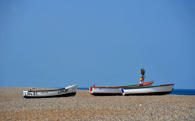 Boat moored on beach against clear blue sky