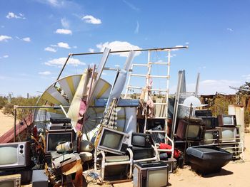 Various abandoned objects in junkyard against blue sky